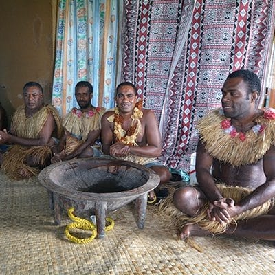 Fijian men in traditional costume around a kava tanoa during kava ceremony.